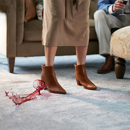 Red wine spilled on carpet beside a woman standing in a living room.