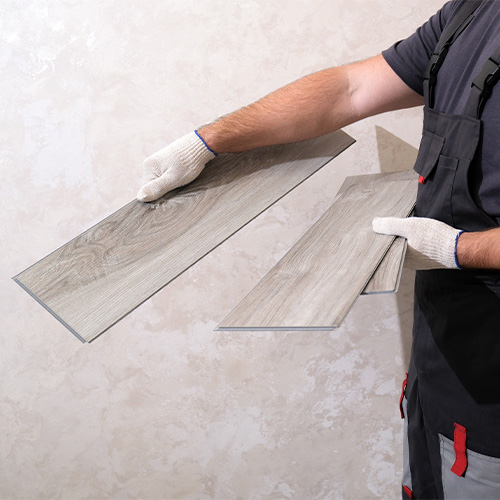 Flooring installer holding wood-look plank flooring during installation.